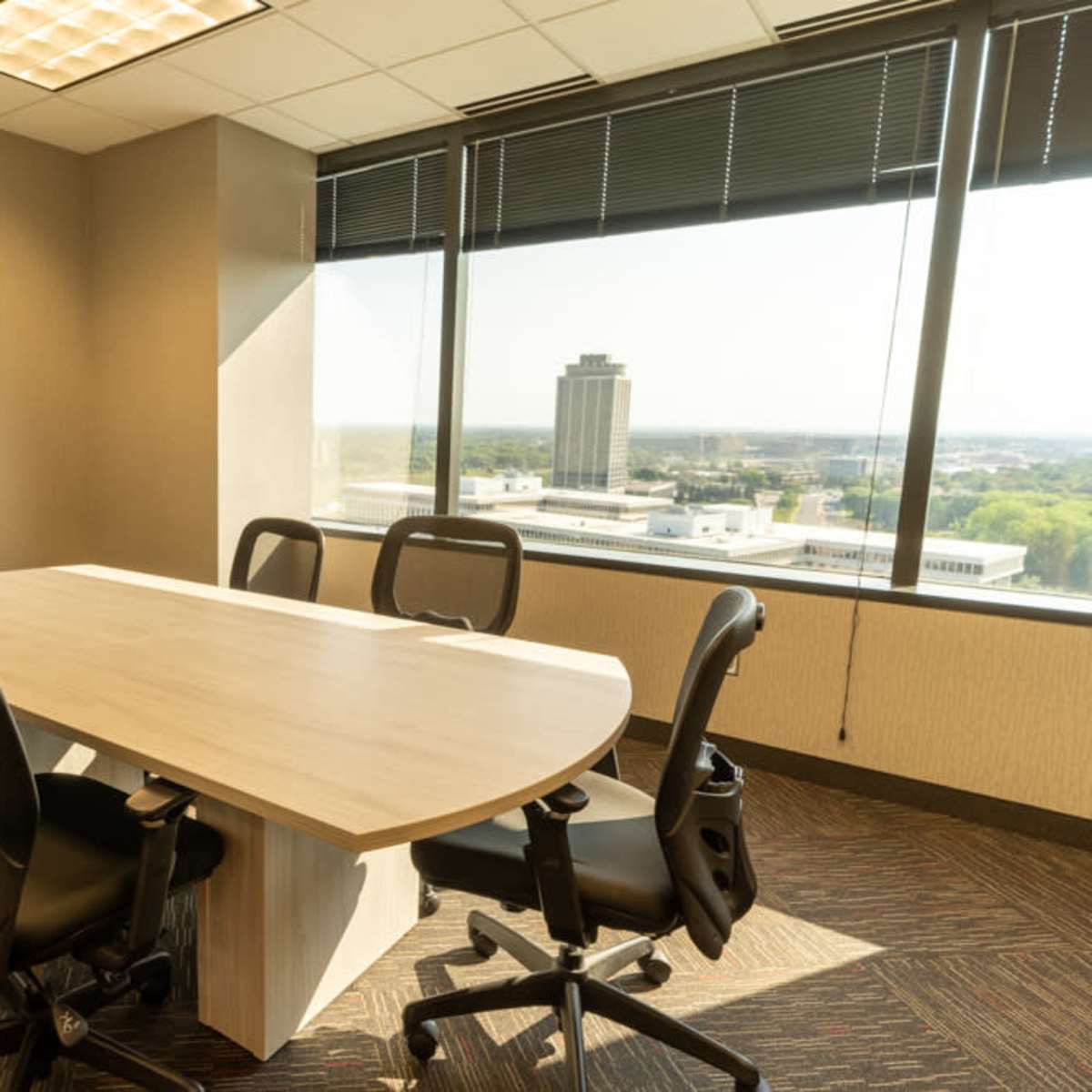 A conference room features a large oval table surrounded by six black chairs and a window with a view of a city skyline.