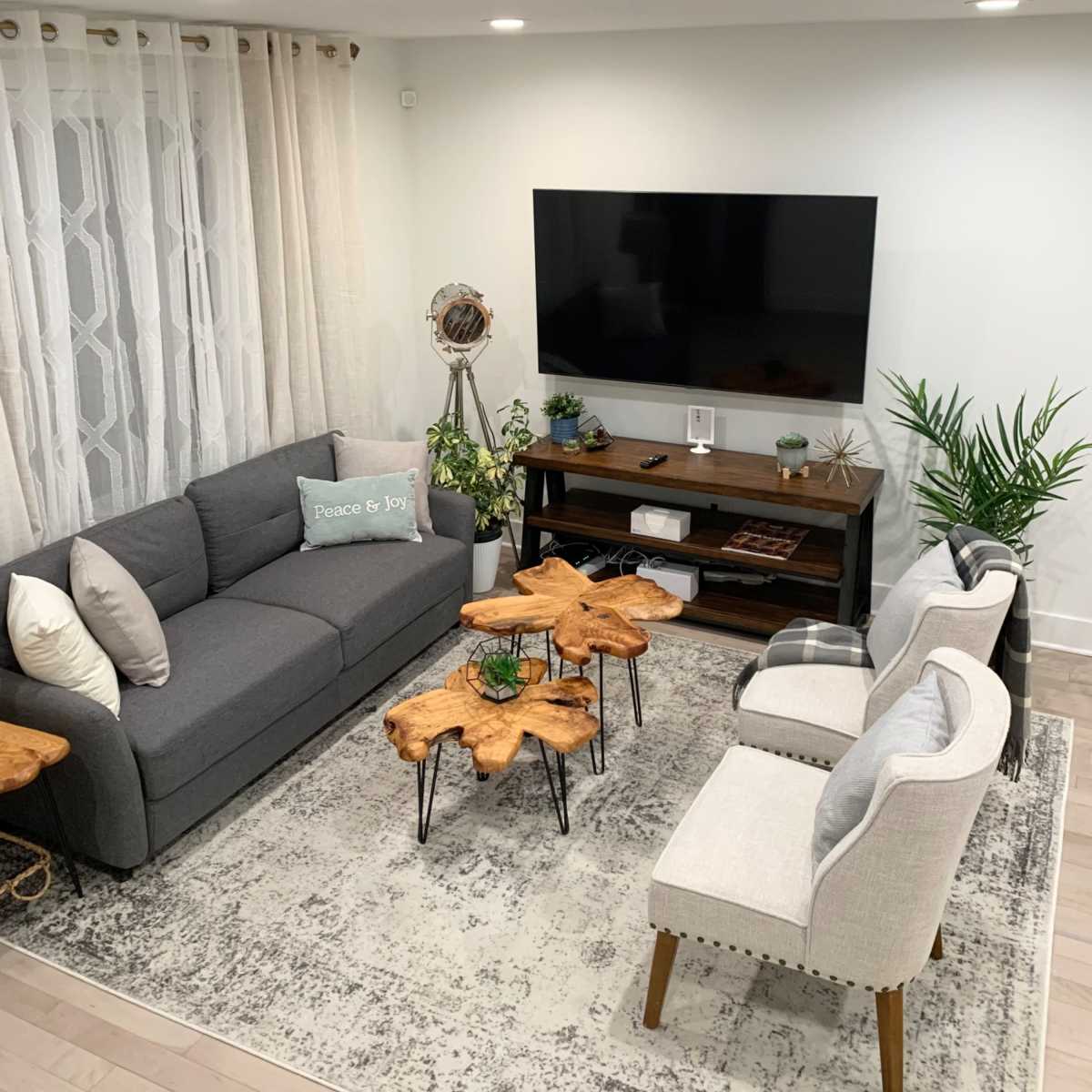 The living room features a gray sofa and two light-colored chairs arranged around wooden coffee tables on a patterned rug, with a television mounted on the wall.