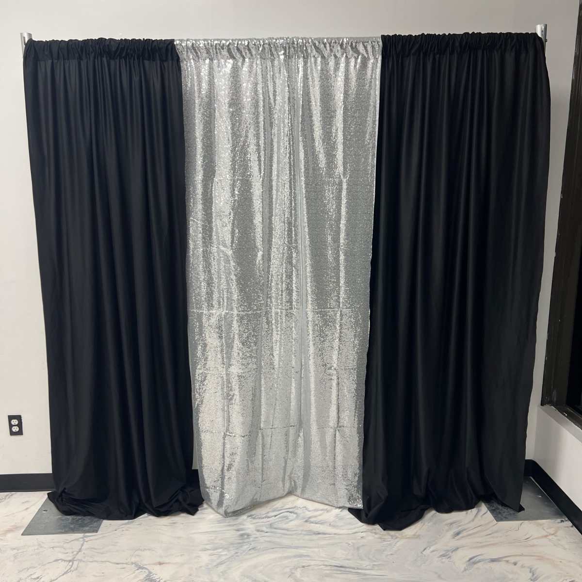 A backdrop consisting of black curtains on either side and a center panel of silver sequined material.