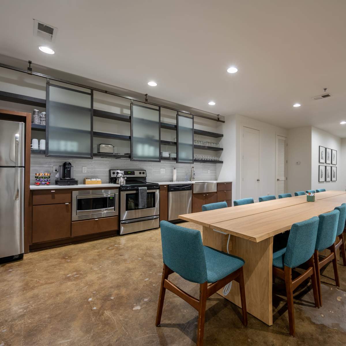 A modern kitchen and dining area featuring stainless steel appliances, a long wooden table with teal chairs, and a minimalist decor style.