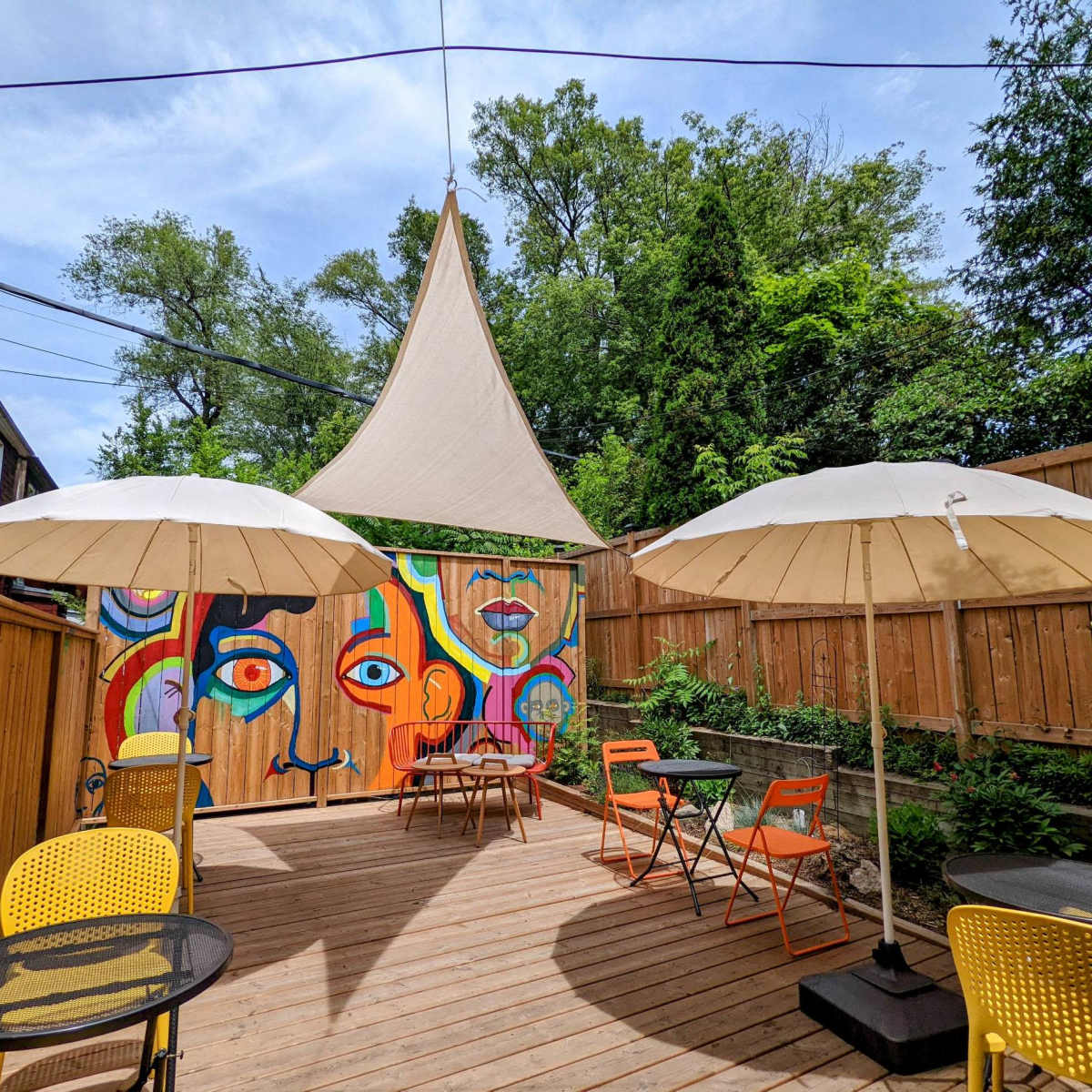 A vibrant outdoor patio features colorful murals, two large umbrellas, and a wooden deck surrounded by greenery.