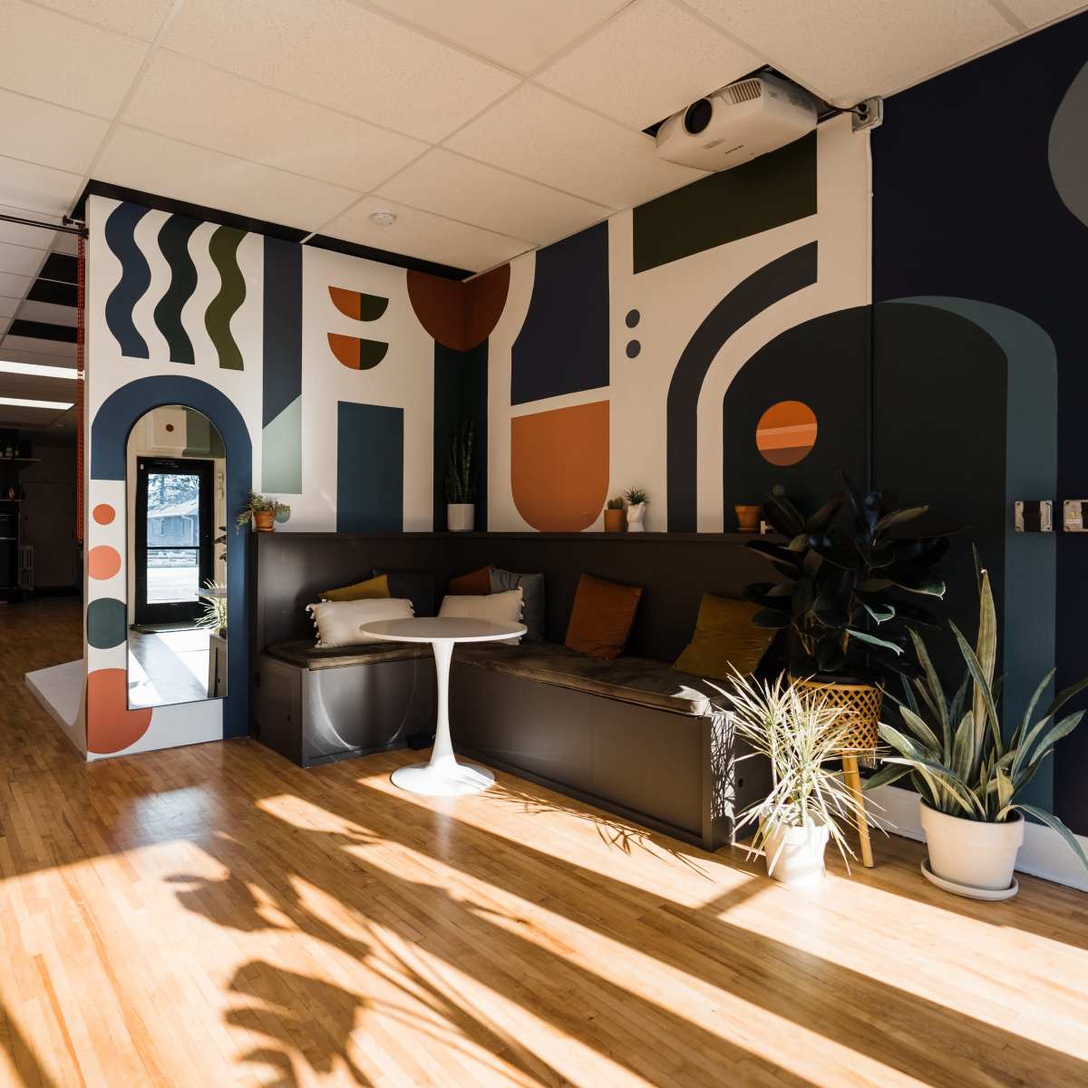 A brightly lit room featuring a modern design with colorful abstract wall art, a black couch, and potted plants.