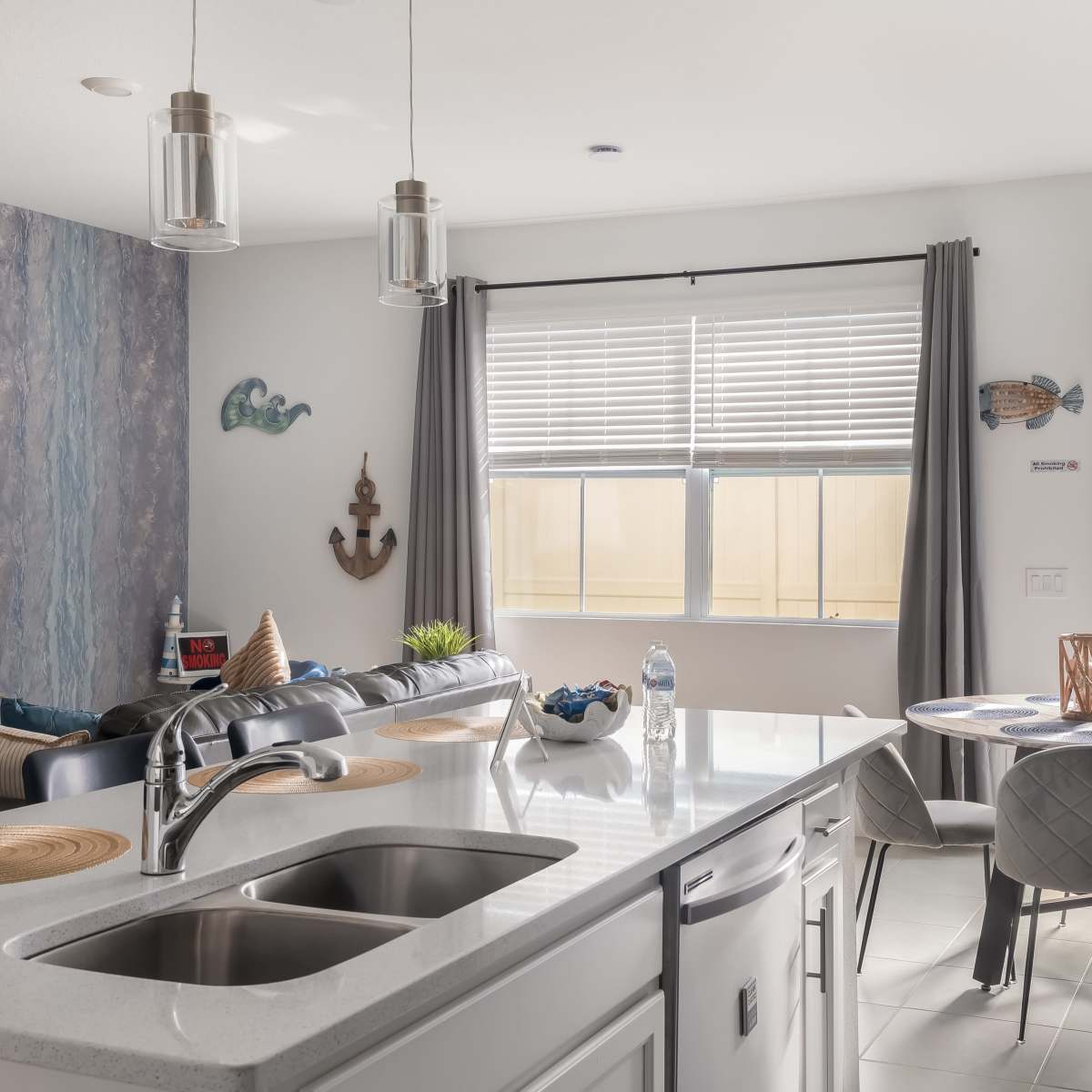 A modern kitchen features a central island with a sink, a dining area with a round table, and large windows providing natural light.