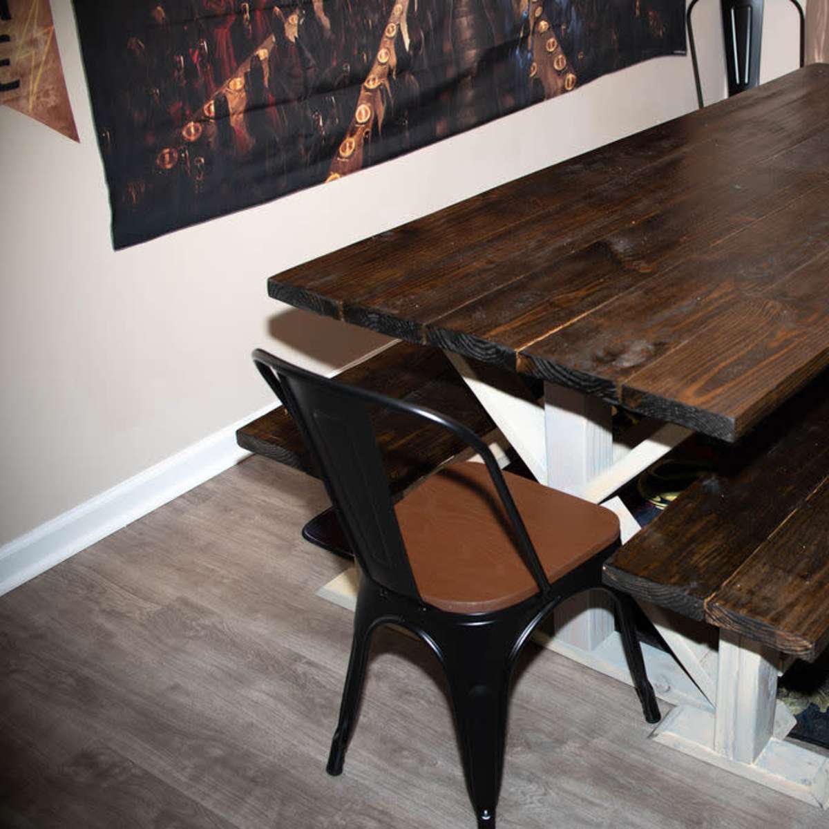 A wooden dining table with two matching benches and a single chair positioned nearby, set against a wall adorned with a decorative poster.
