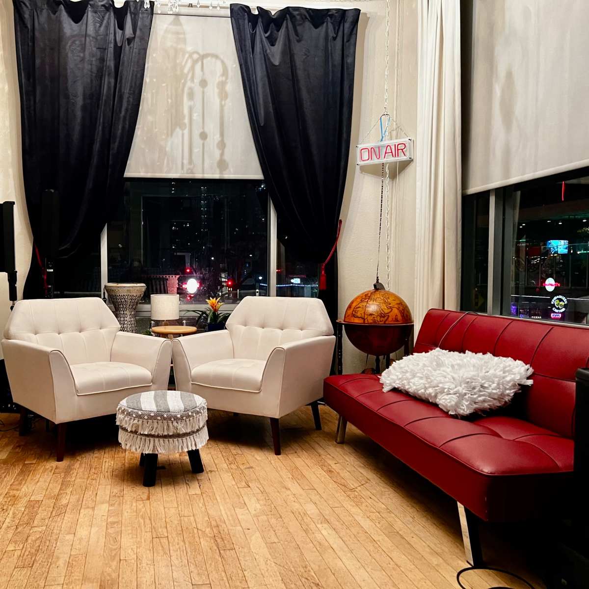 A cozy room with two white armchairs, a red sofa, a small round table, guitars on display, and large curtains framing a window.