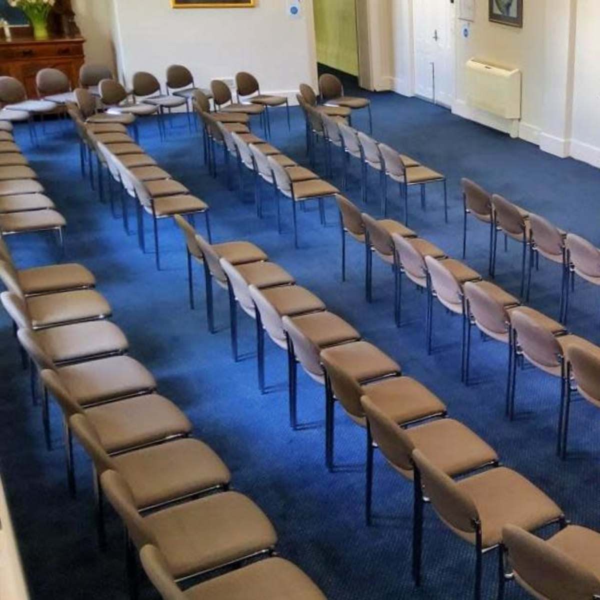 A room set up for a meeting with rows of chairs facing a blank screen and a small table at the front.