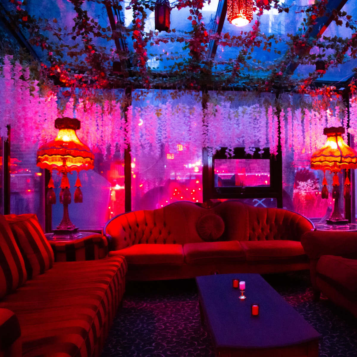 The scene features a dimly lit lounge area with red and purple lighting, adorned with floral decorations and vintage lamps.