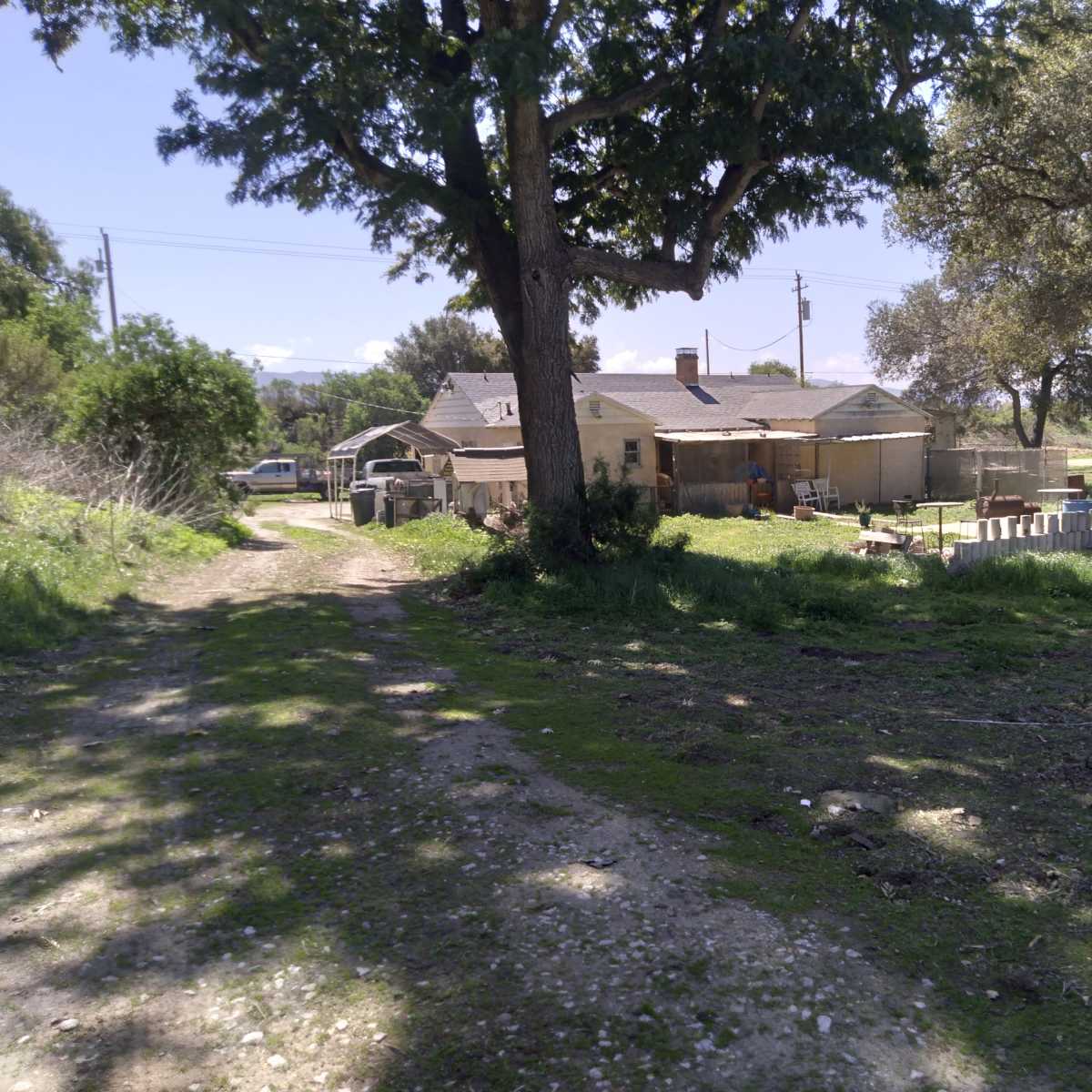 A dirt path leads towards a cluster of buildings surrounded by trees and open land.