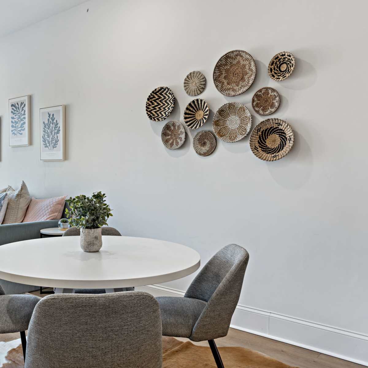A modern living room featuring a sofa, decorative wall art made of woven plates, and a round dining table with gray chairs.