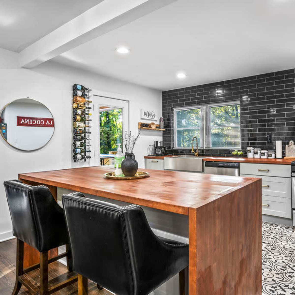 A modern kitchen features stainless steel appliances, a wooden island, and patterned tile flooring, with wine racks and a round mirror on the walls.