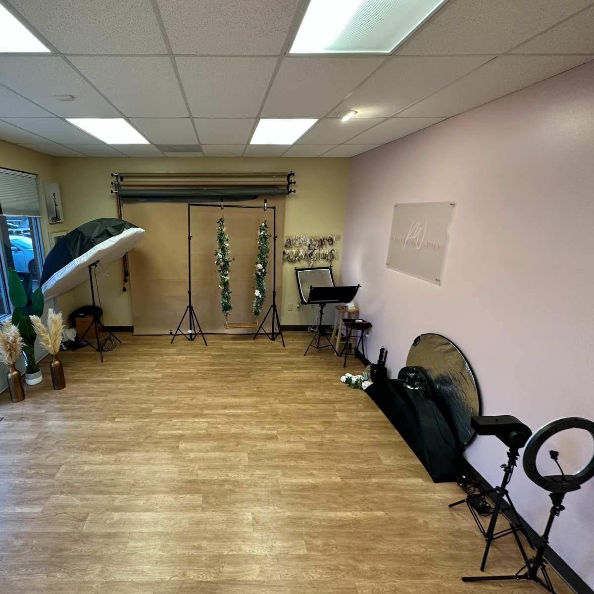 A well-lit studio space featuring photography equipment, including softbox lights, backdrops, and decorative plants, along with a seating area.