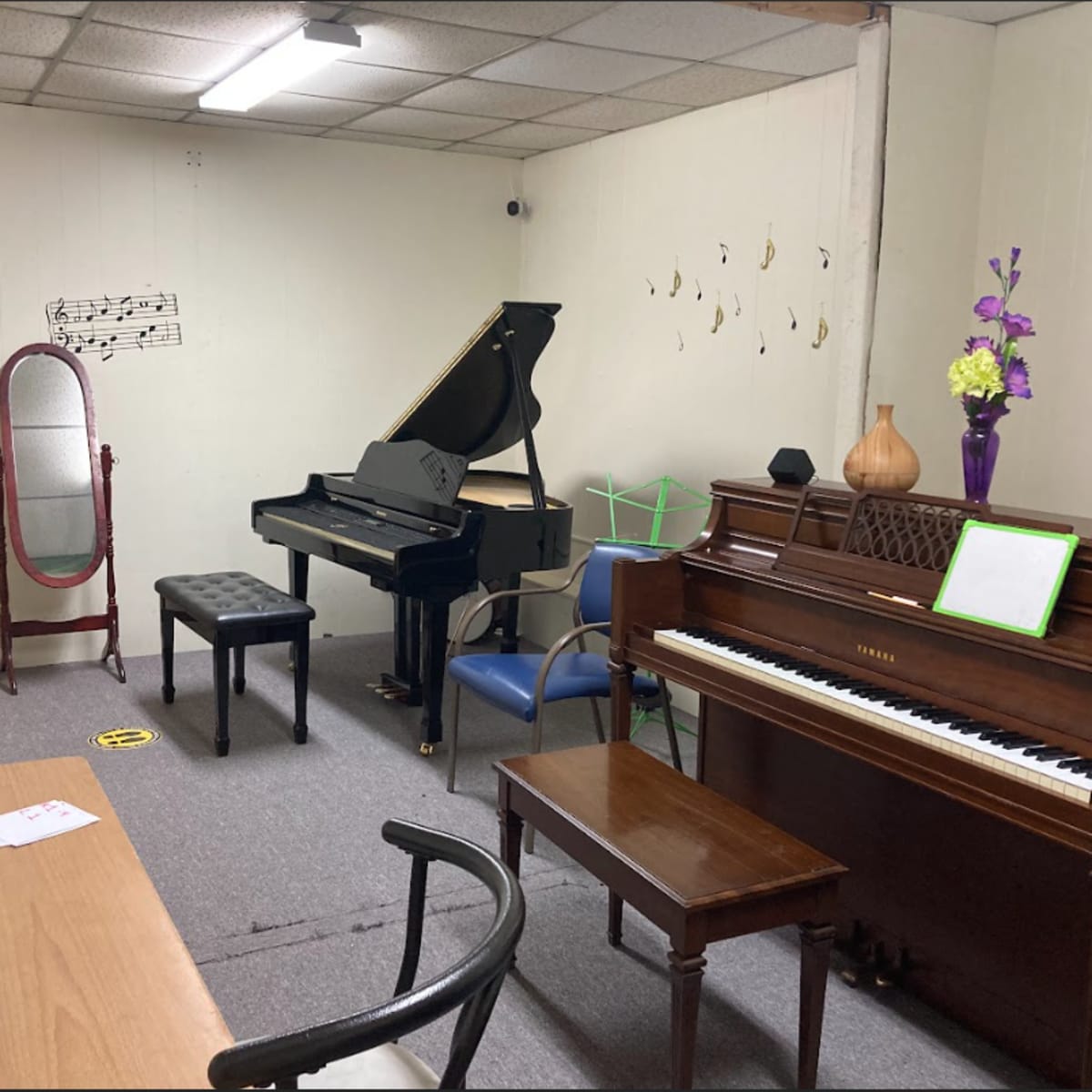 The room contains two pianos, a mirrored stand, a music stand, a table, and decorative elements, all arranged with musical notes on the walls.