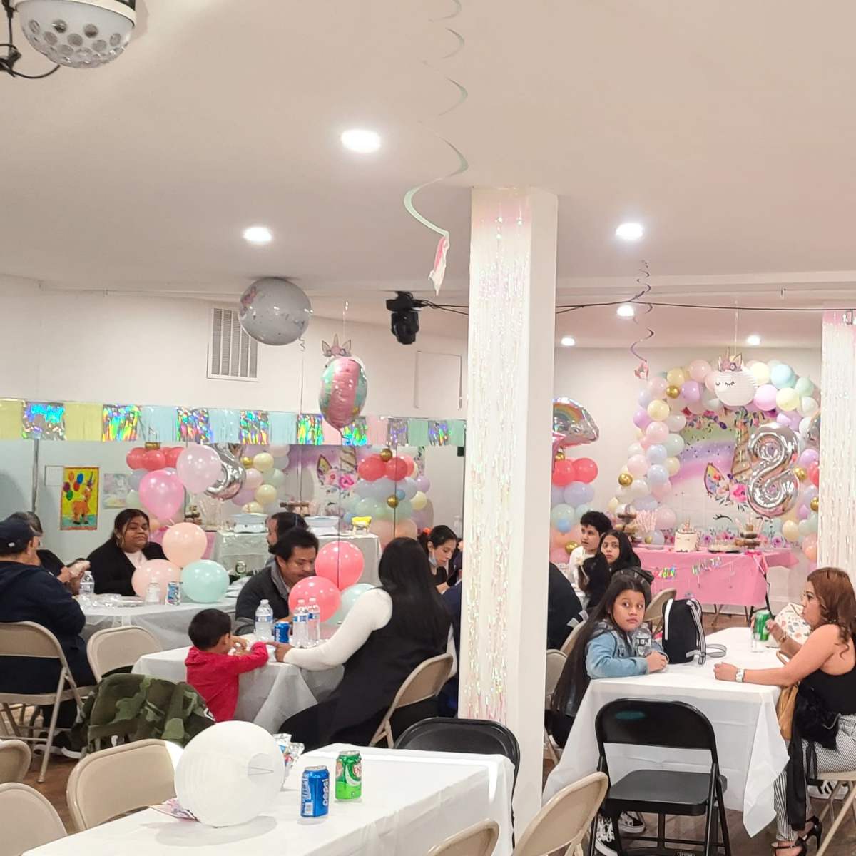 A decorated indoor party space with tables, chairs, colorful balloons, and a bounce house in one corner.