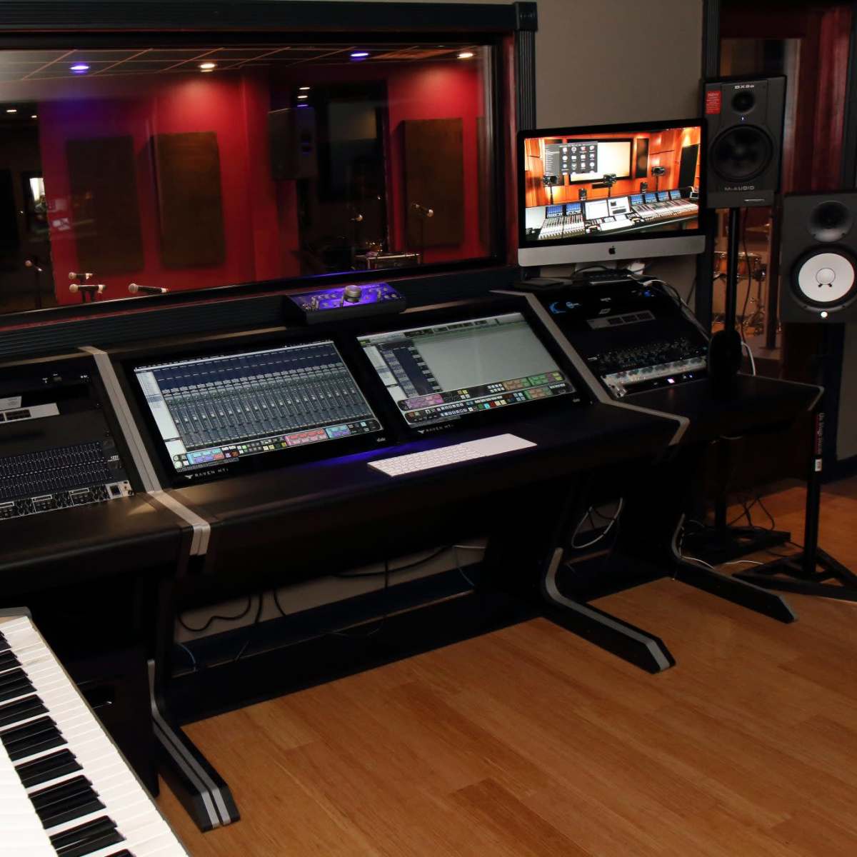 A modern music studio with a keyboard, multiple sound mixing consoles, and monitors arranged on a sleek desk.
