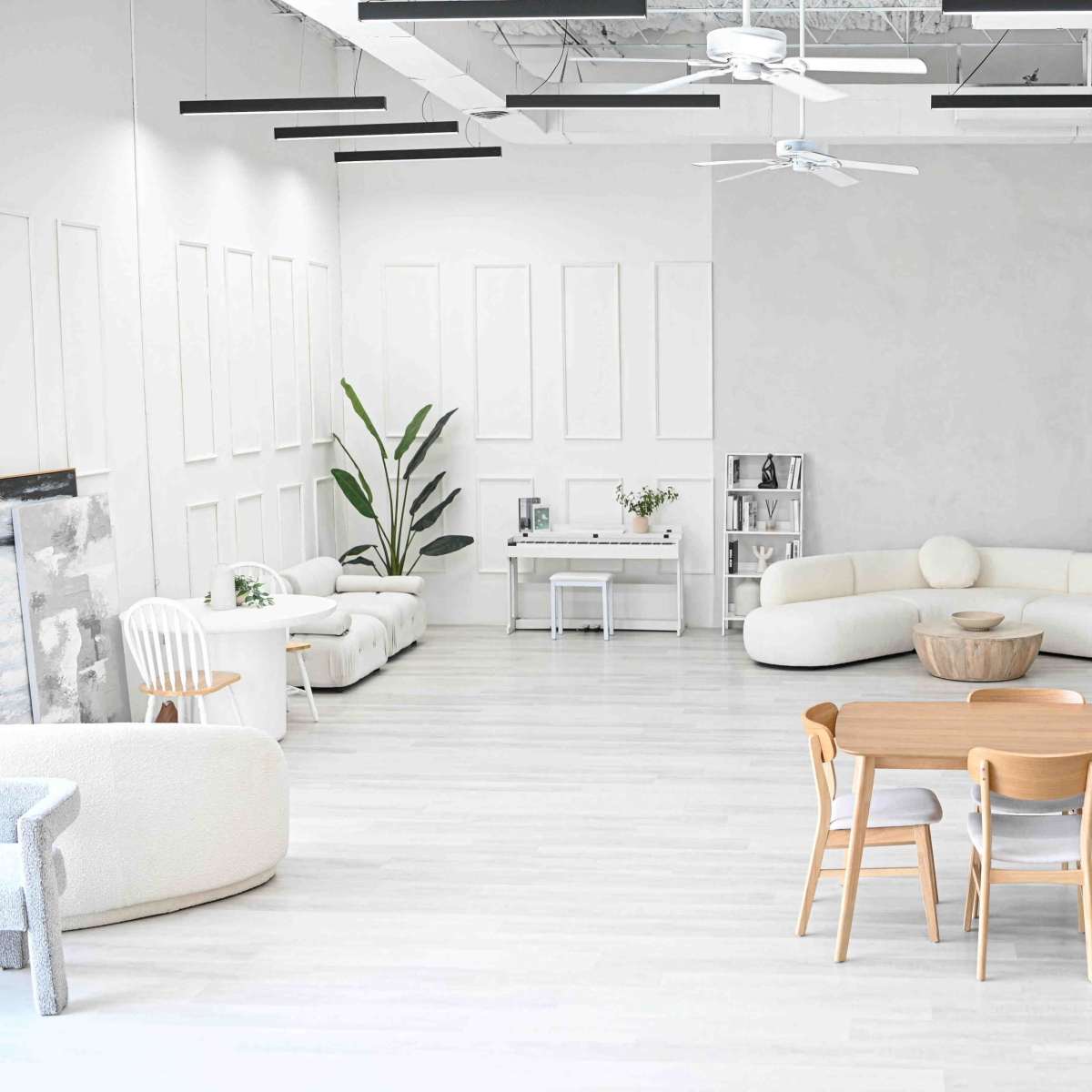 A spacious, modern interior with light-colored flooring, several seating areas, and a wooden table surrounded by chairs.