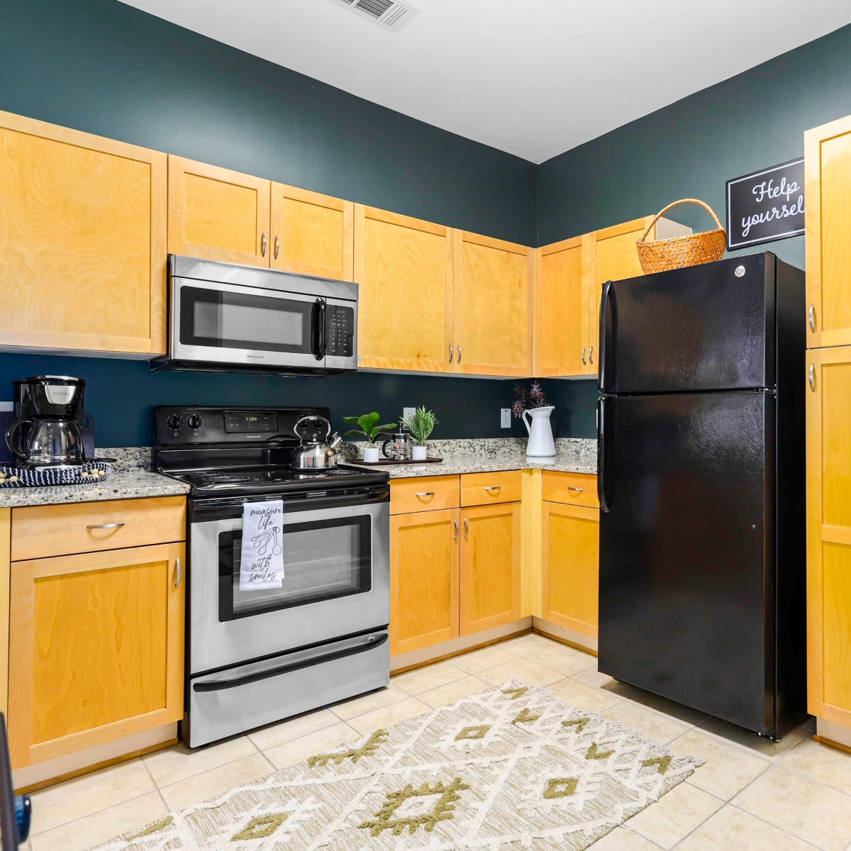 A compact kitchen with wooden cabinets, a black refrigerator, stainless steel appliances, and a granite countertop.