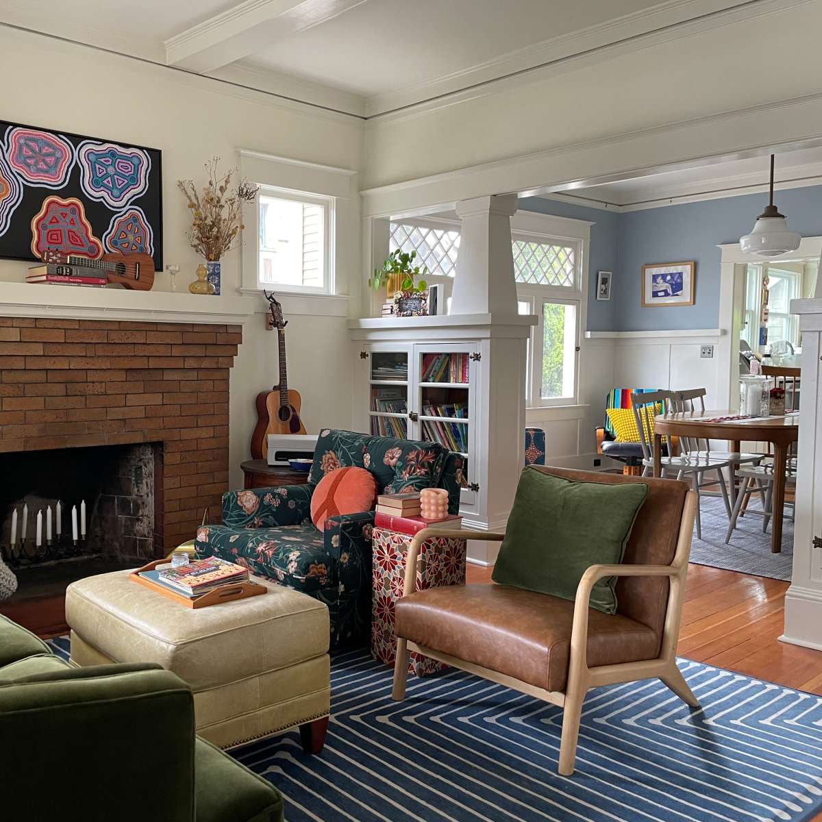 A cozy living room features a brick fireplace, patterned furniture, and an adjoining dining area with colorful chairs.