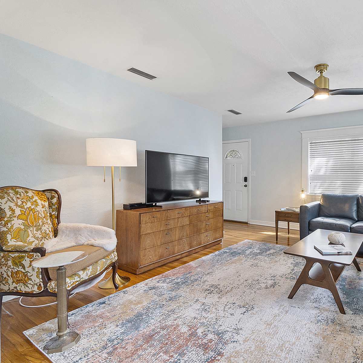 A well-furnished living room with a sectional couch, a wooden television stand, a coffee table, and large windows allowing natural light.