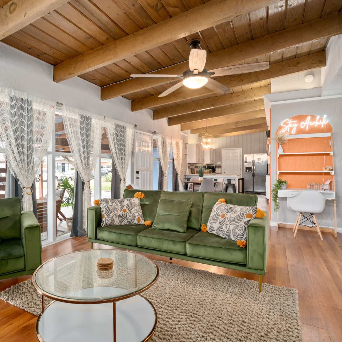 A bright living room with green sofas, wooden beams on the ceiling, and a round coffee table in front of large windows.