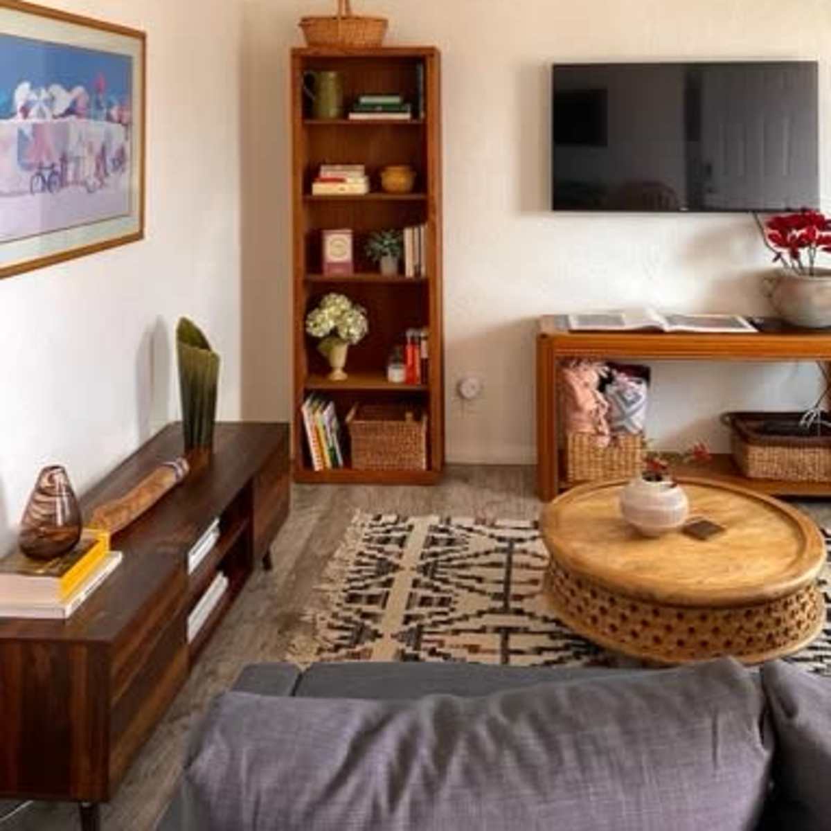 A modern living room featuring a wall-mounted TV, a wooden coffee table, a console table, and a bookshelf filled with books and decorative items.
