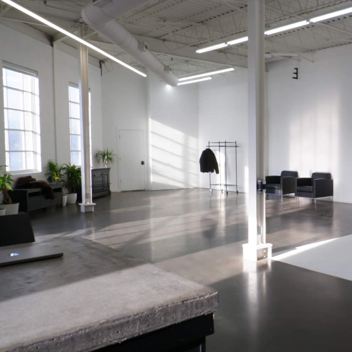 A spacious, bright studio with a polished concrete floor, a white backdrop, and minimalist furniture including a coat rack and two black chairs.