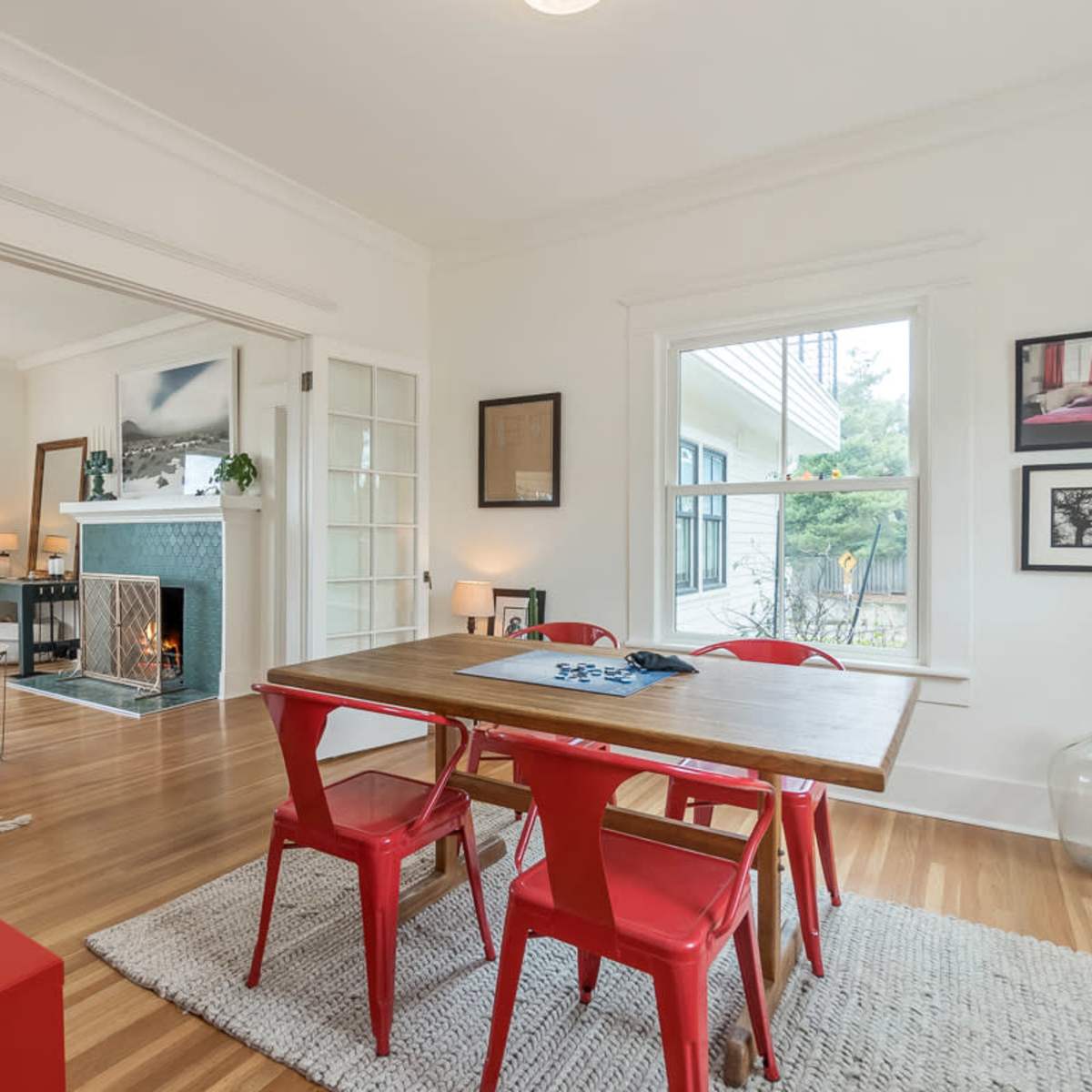 A dining area with a wooden table surrounded by red chairs, open to a living space featuring a fireplace and artwork on the walls.