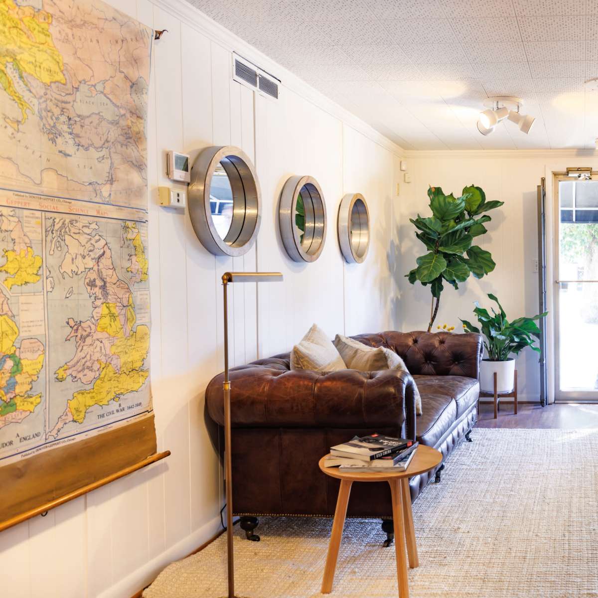 A cozy entryway with a leather couch, a potted plant, mirrors on the wall, and a wooden bench near a glass door.