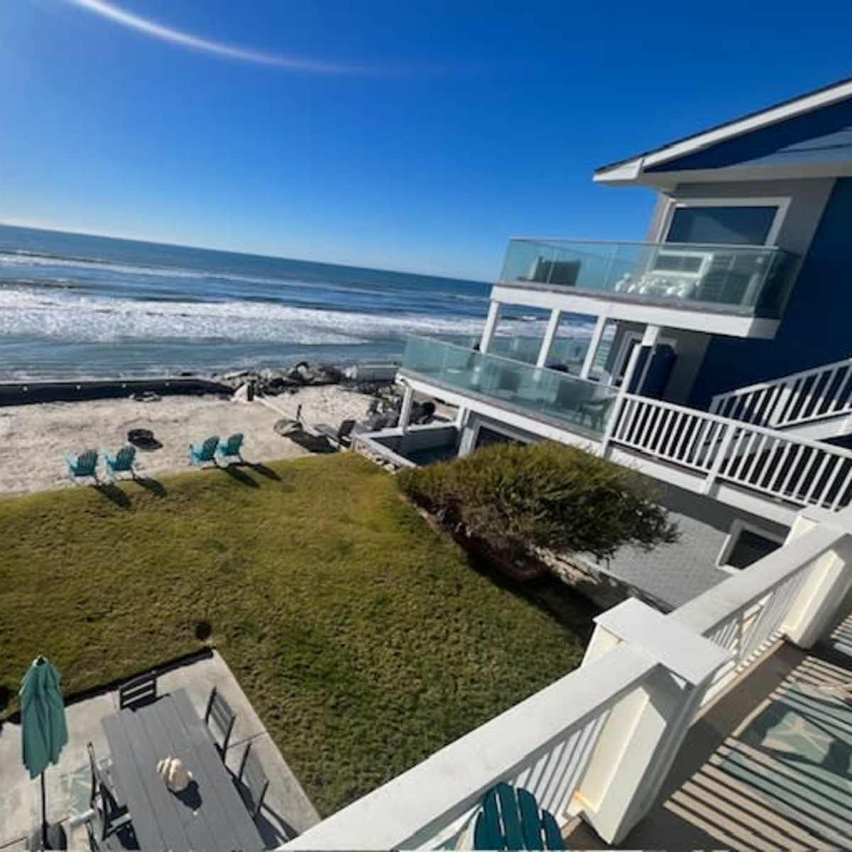 A beachfront property with green lawn furniture, overlooking the ocean and a sandy beach.