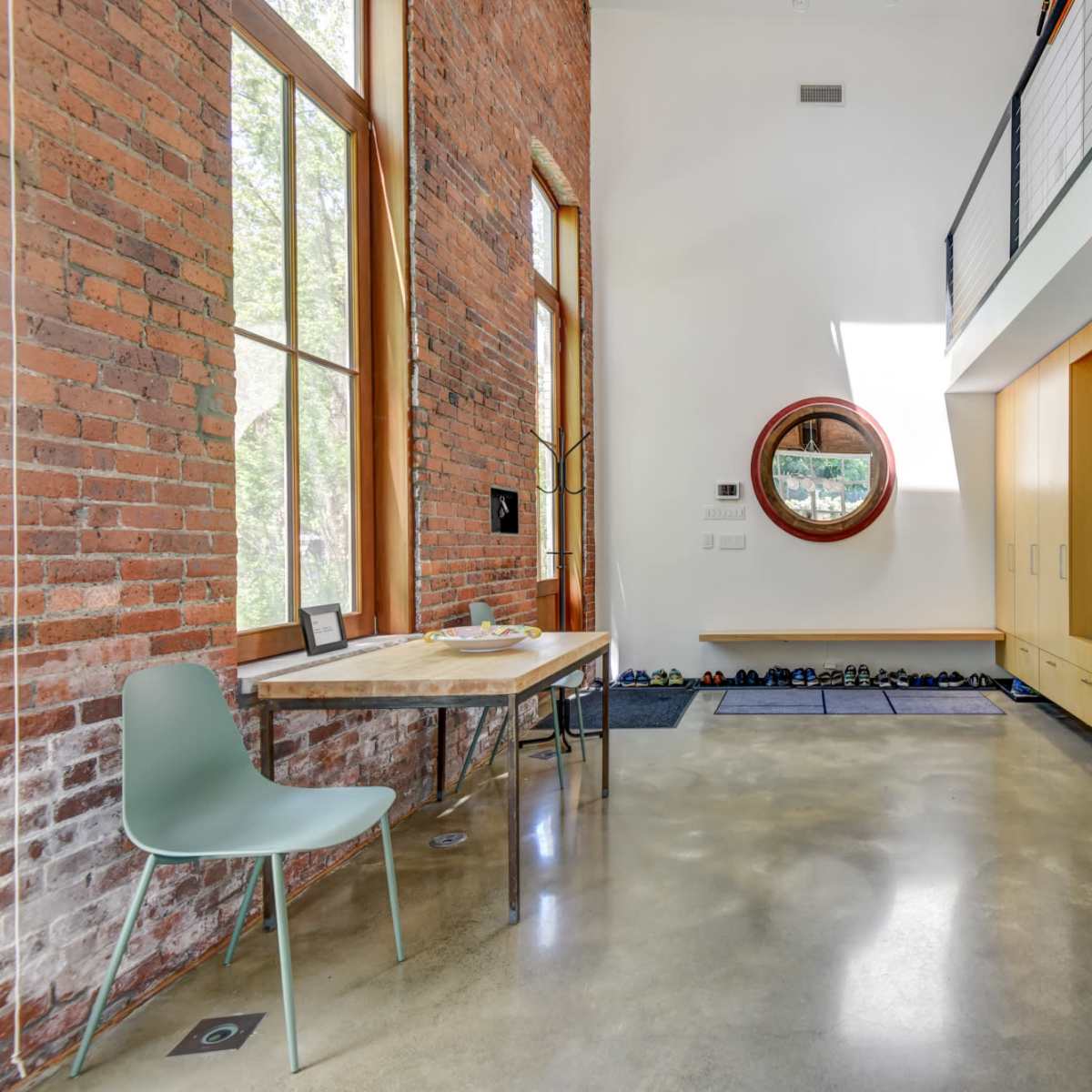 A spacious interior features a wooden dining table and a green chair alongside a built-in storage unit and large circular window.