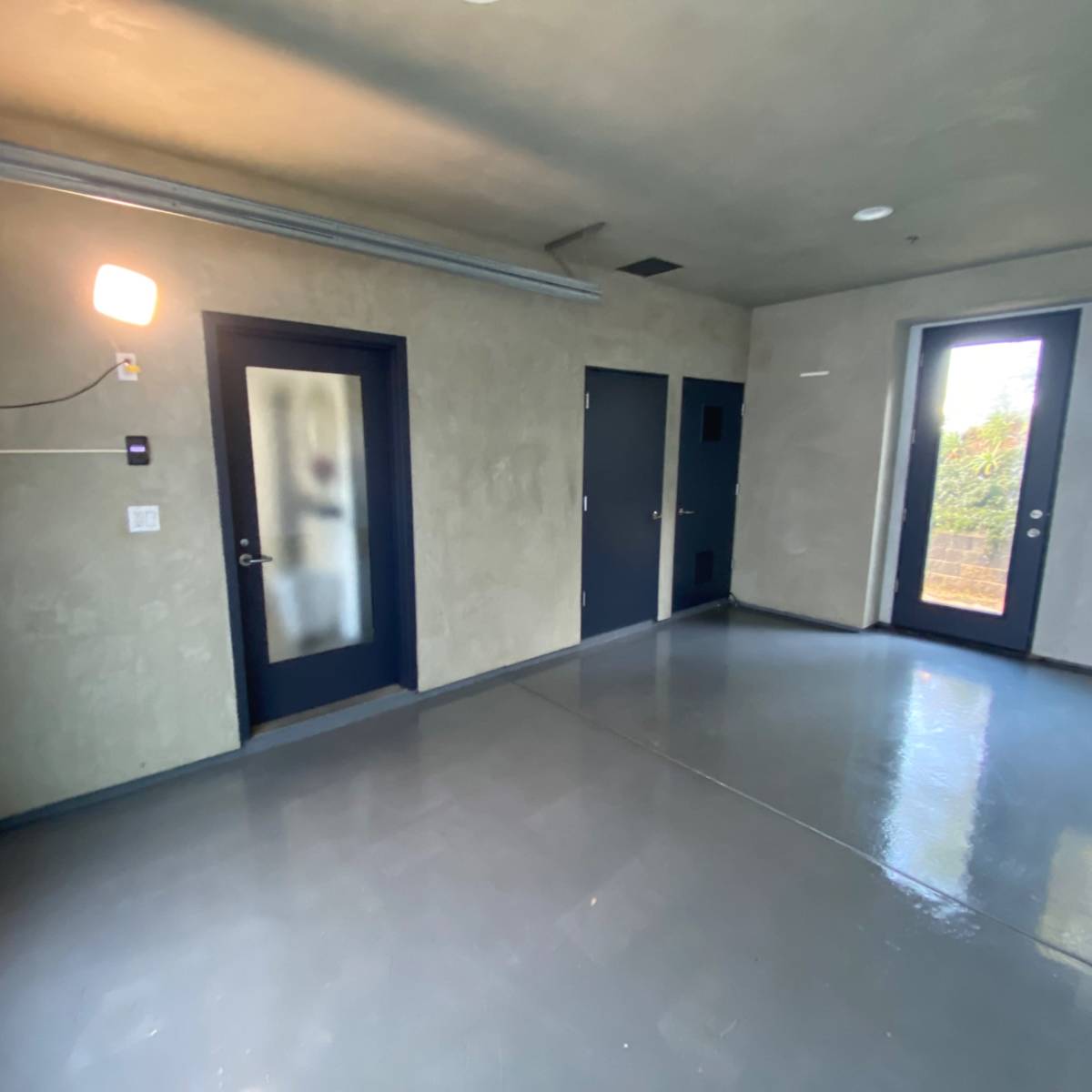 A minimalist, empty room with concrete walls, a polished floor, and two doors leading outside.