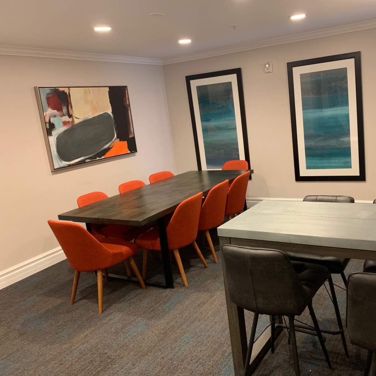 The room features a dining area with a long table surrounded by orange chairs, complemented by two framed artworks on the walls.