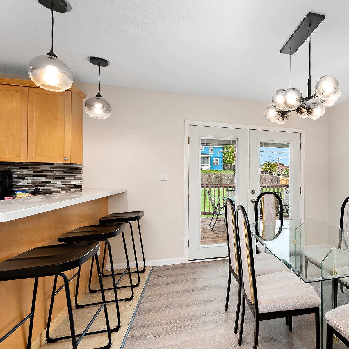 A modern dining area features a glass table surrounded by black chairs, with a bar counter and pendant lights above.