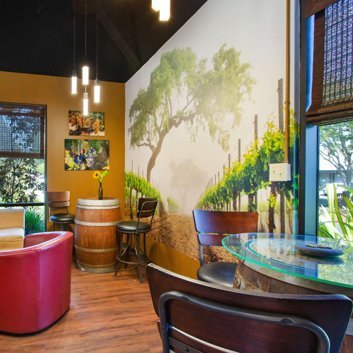 A cozy seating area with a curved couch, a round table, and a wine barrel against a mural of vineyard scenery on the wall.