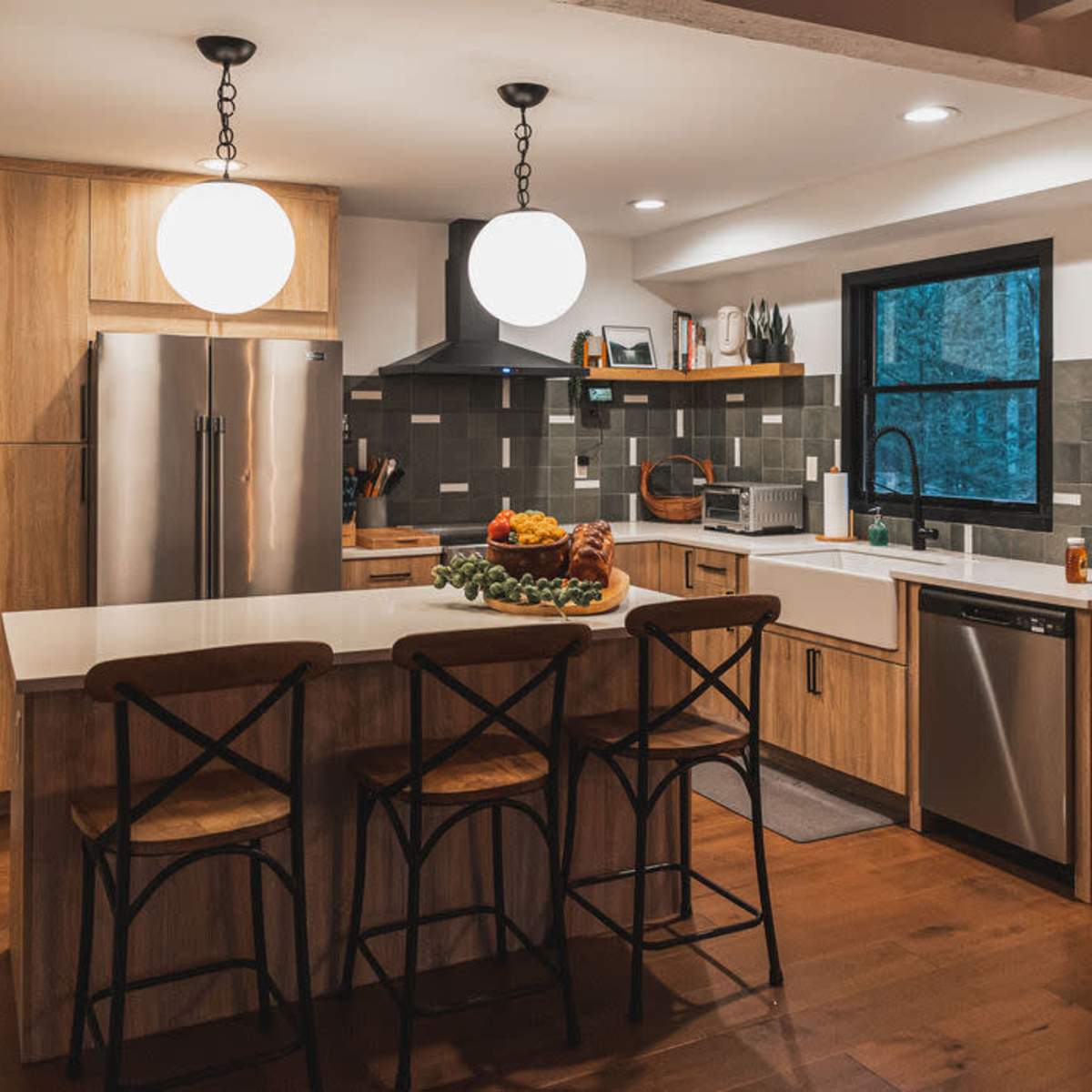 A modern kitchen with wooden cabinets, a large island with a fruit centerpiece, and stainless steel appliances.