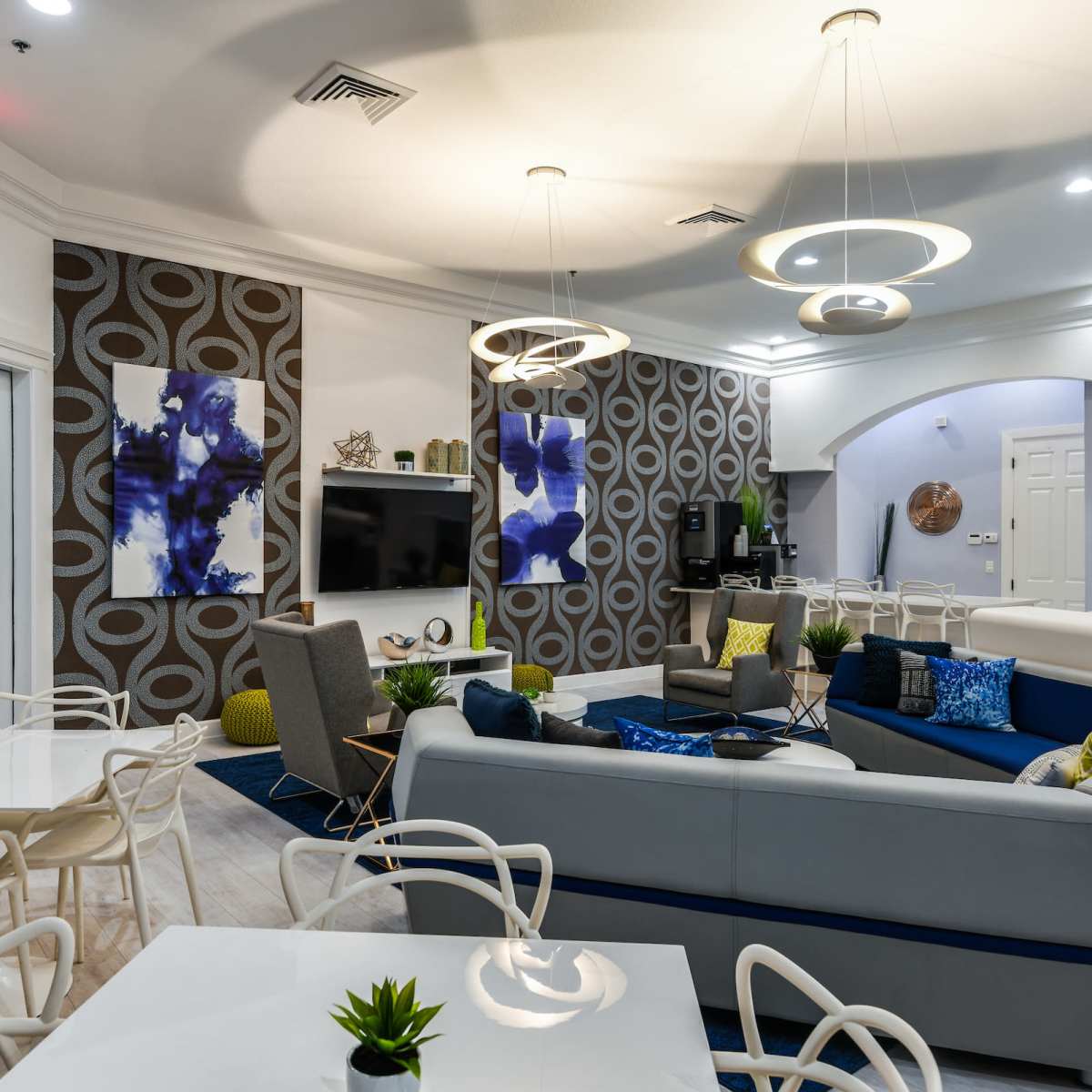 A modern lounge area featuring a large sectional sofa, art on the walls, and several tables and chairs arranged for social gatherings.