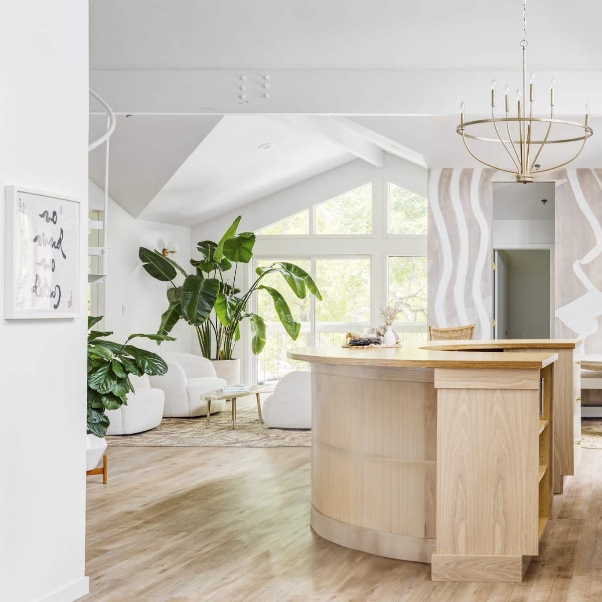 A modern, open-concept interior featuring a light wooden reception desk, large windows filled with natural light, and lush green plants surrounding the space.