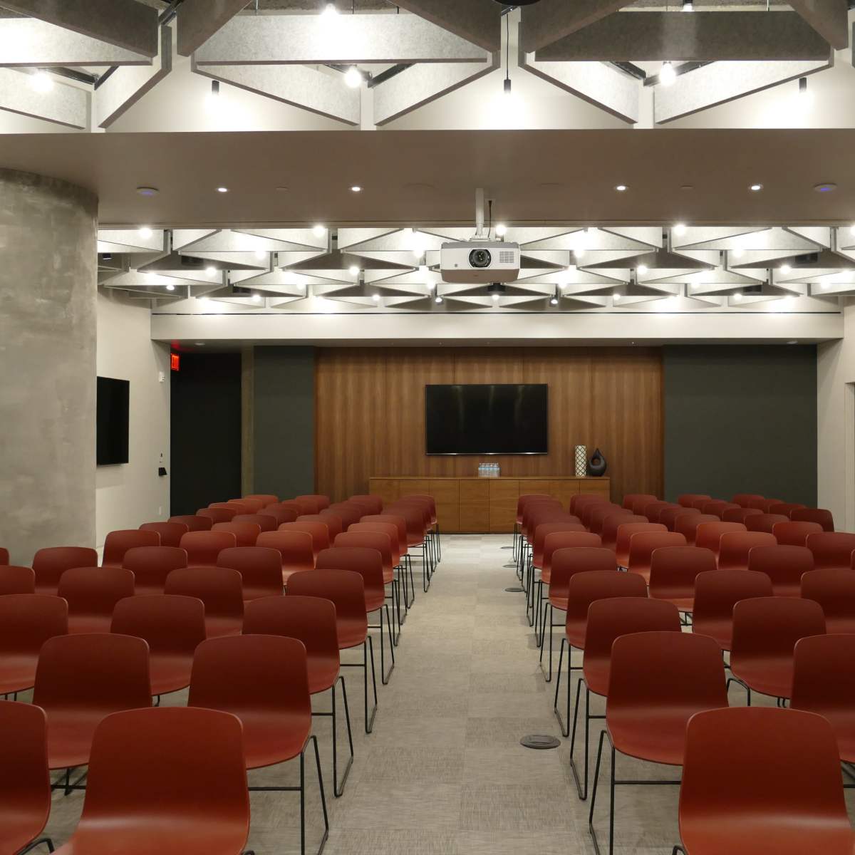 A conference room set up with rows of red chairs facing a wooden wall with a television and projector.
