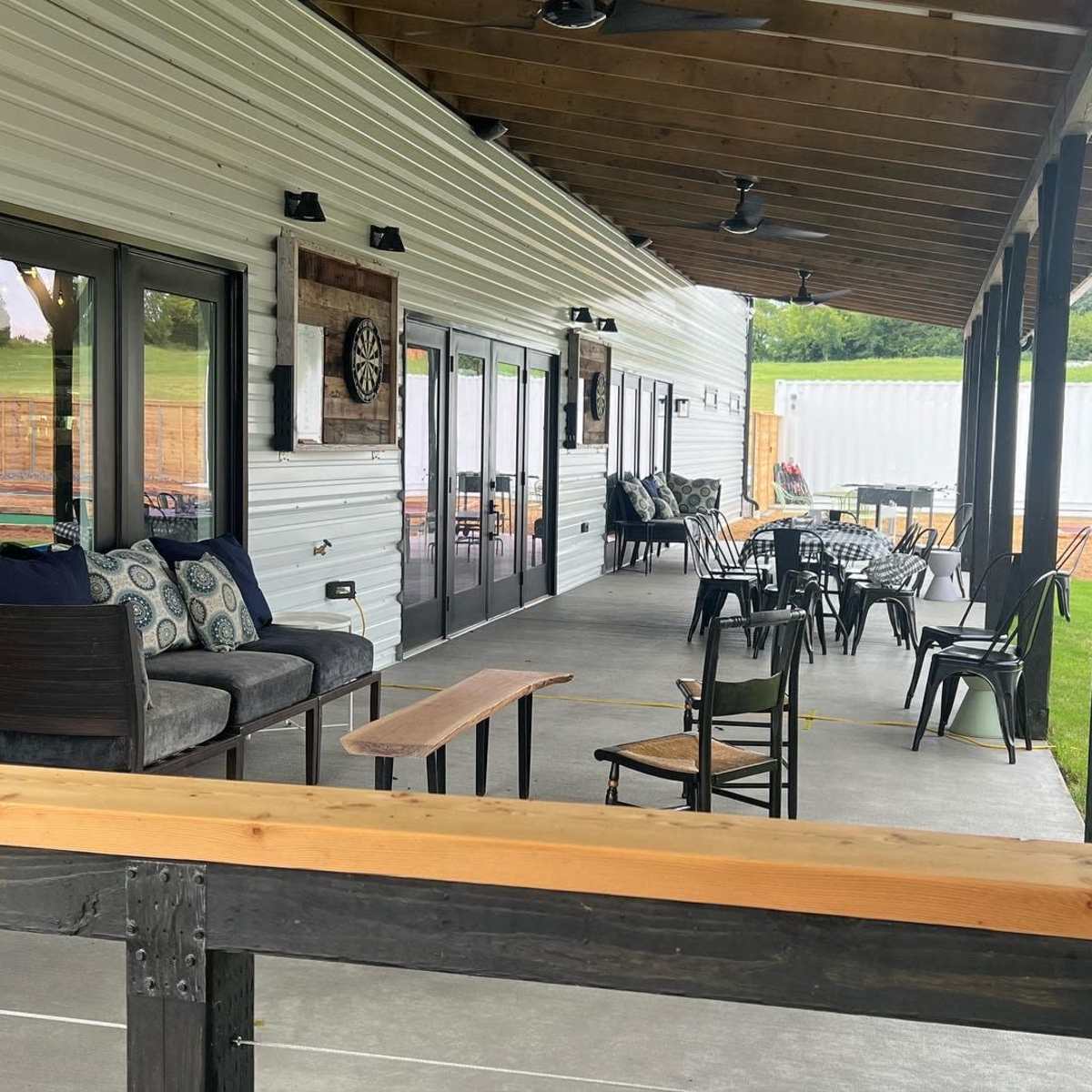 A covered outdoor patio area with various seating options, including couches and chairs, alongside a grassy lawn.