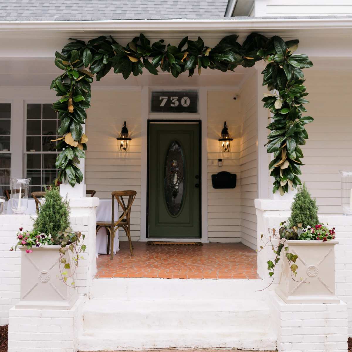 A front entrance features a green door framed by a leafy arch, with decorative planters on either side and brick steps leading up to it.