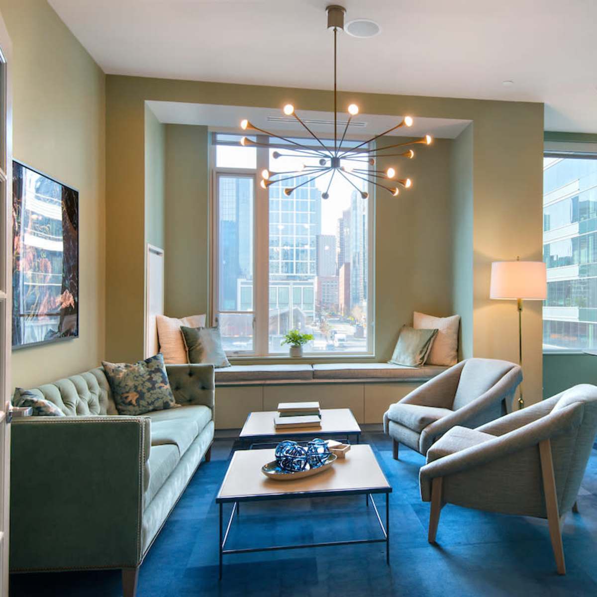 A modern lounge area features a green sofa and two armchairs near a large window with city views.