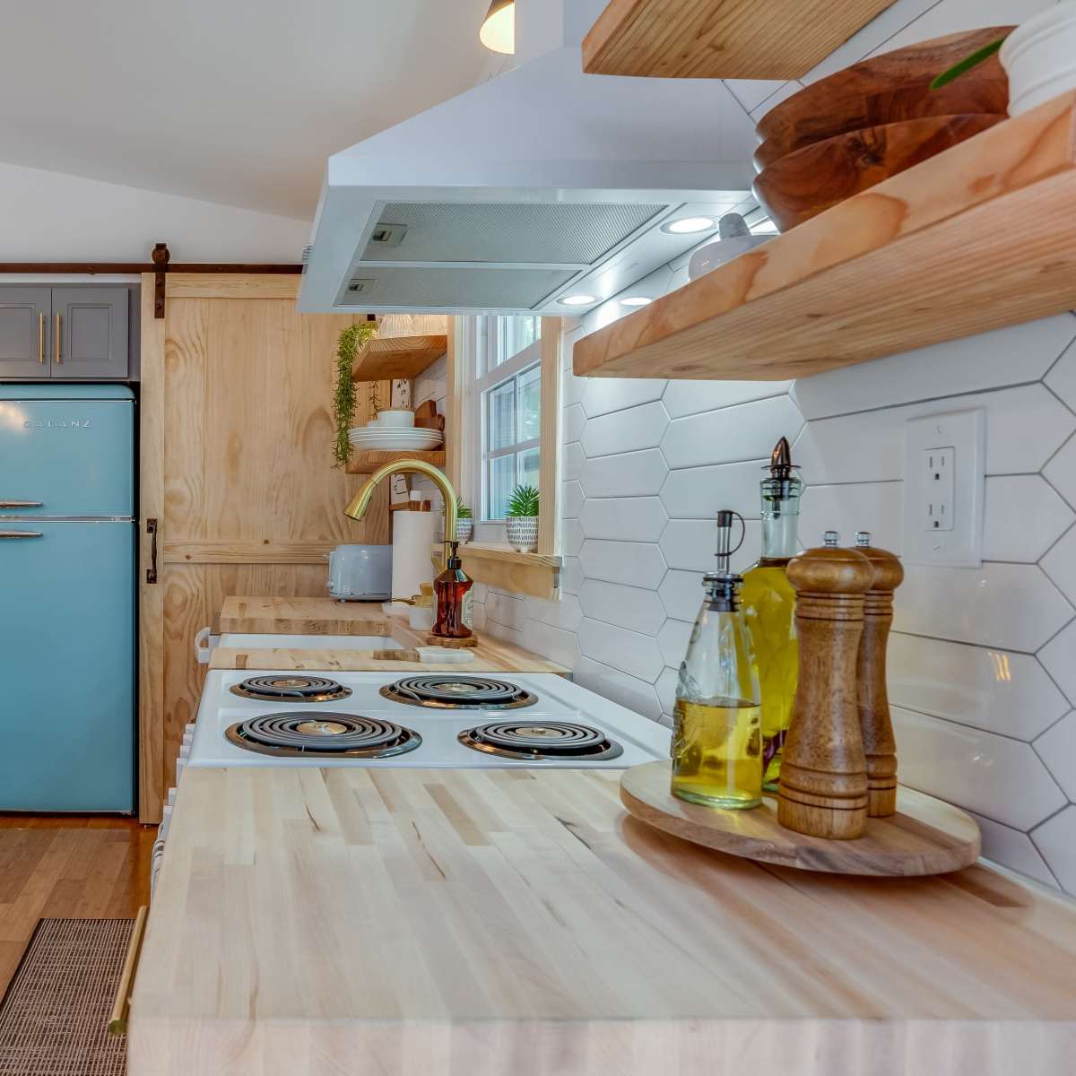 A modern kitchen with light blue cabinetry, a sliding barn door, and wooden shelves displaying kitchen items.