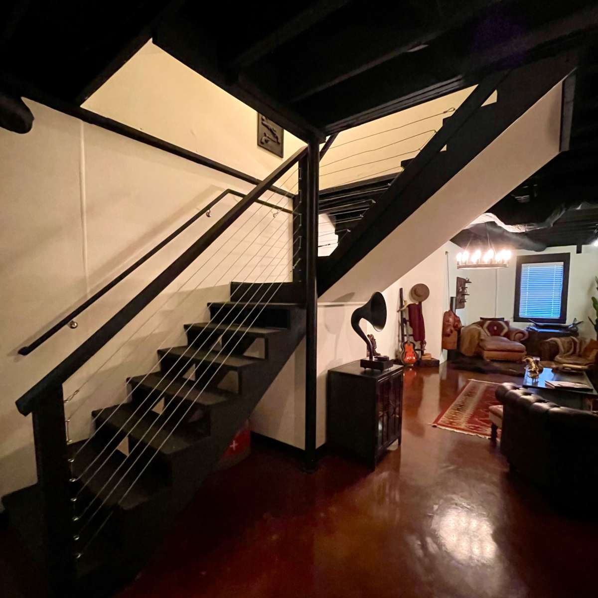 A well-lit staircase with a black railing leading to an upper level, adjacent to a cozy living area with vintage decor.