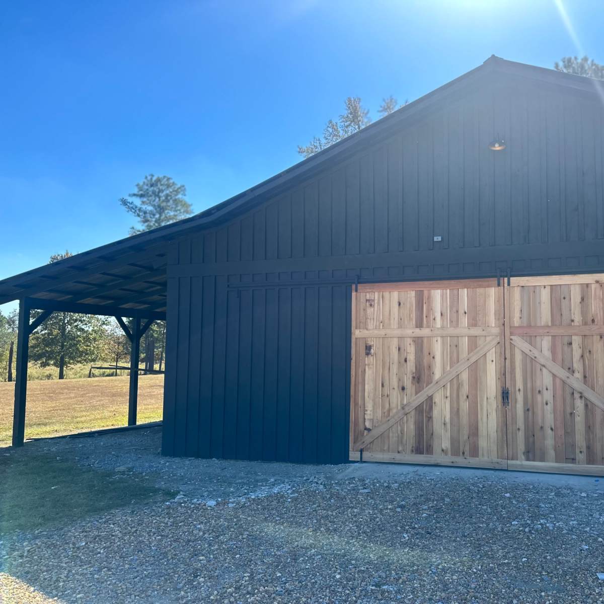 A dark wooden barn with a large wooden double door and a gravel pathway in front of it.