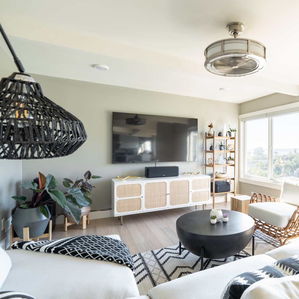 A modern living room featuring a light-colored sofa, a round black coffee table, and large windows with a view of greenery outside.