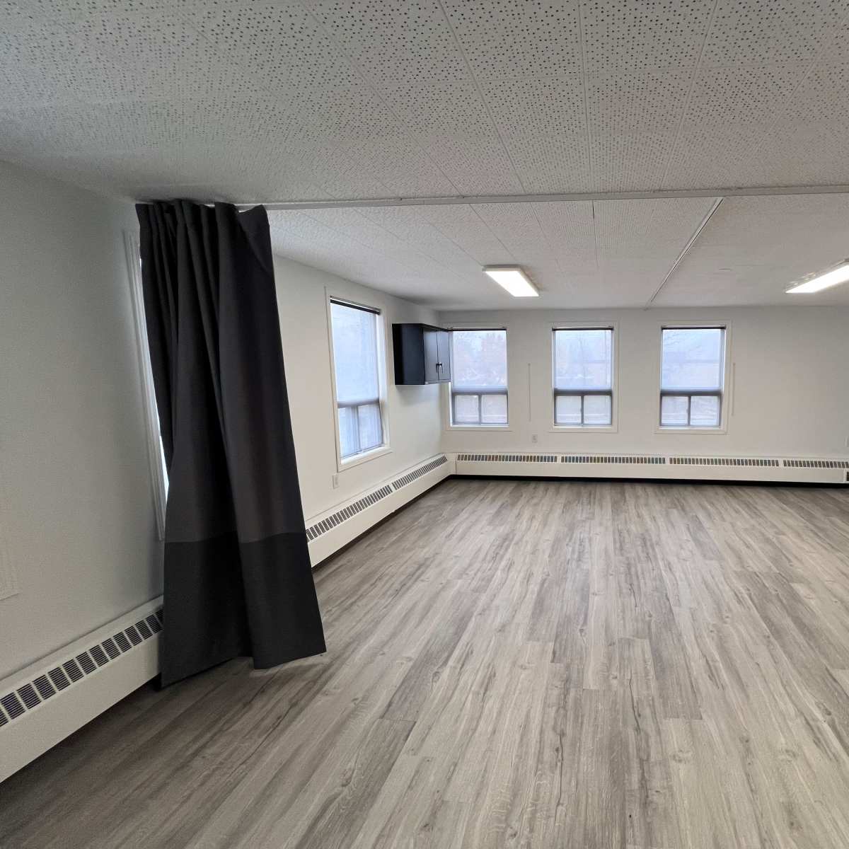 An unfurnished, open room with light wood flooring, large windows, and gray curtains on one side.