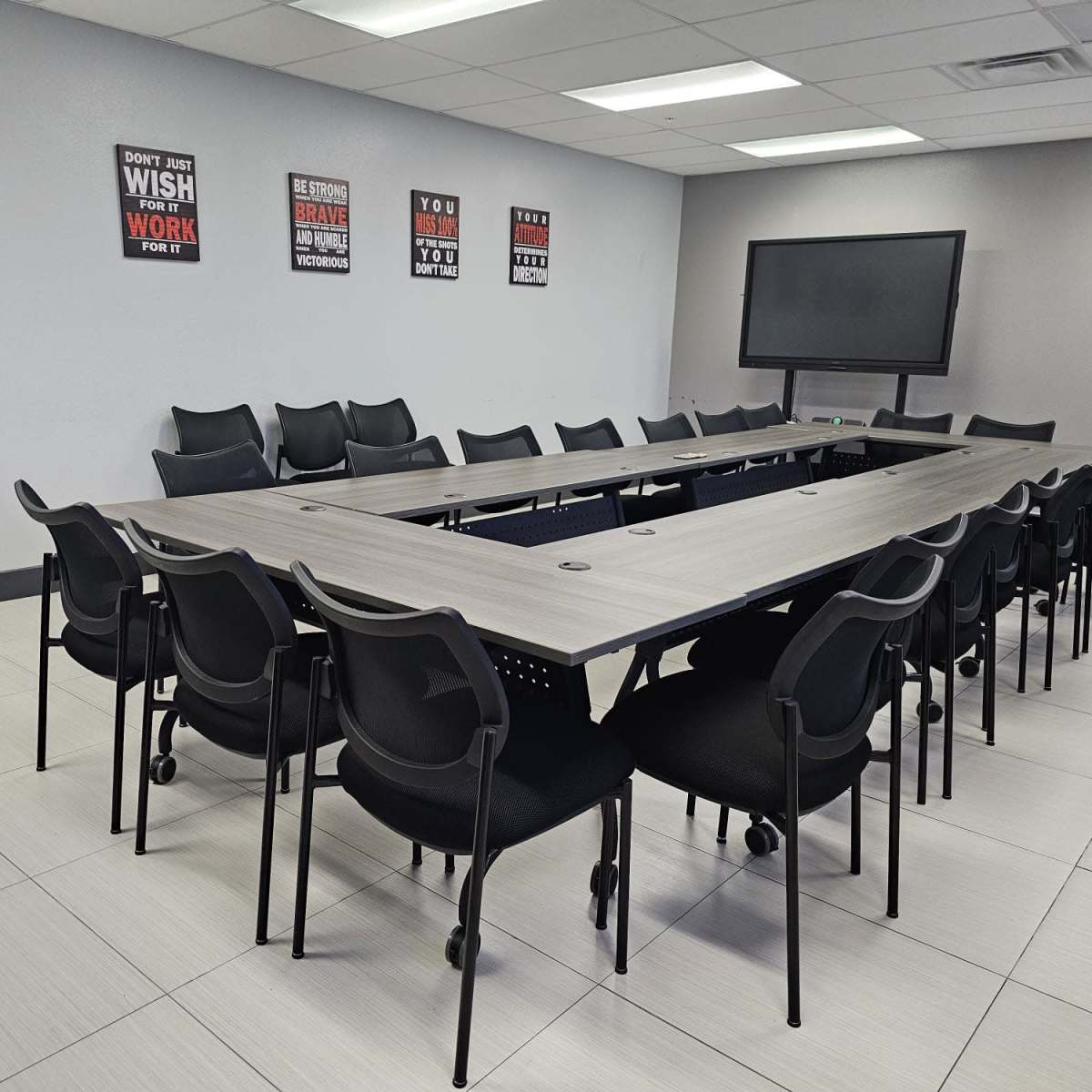 A large conference room features a rectangular table surrounded by black rolling chairs and motivational posters on the walls.