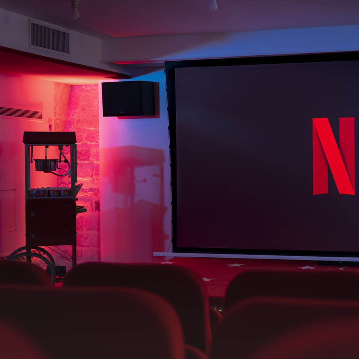 A large screen displaying the Netflix logo is set up in a dimly lit movie theater with red seating.