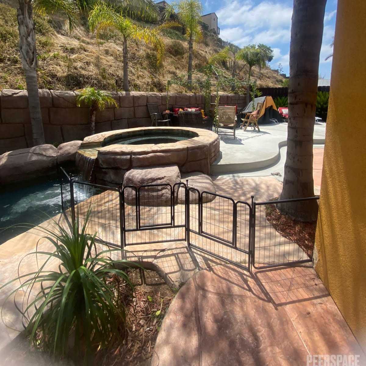 A backyard pool area with a hot tub, palm trees, and a fenced-off section on a sunny day.