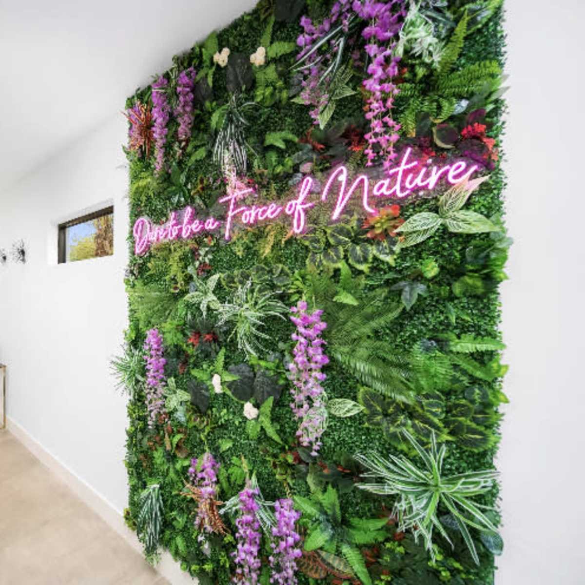 A modern hallway featuring a prominent vertical garden with vibrant plants and a neon sign that reads "Embrace a Piece of Nature."
