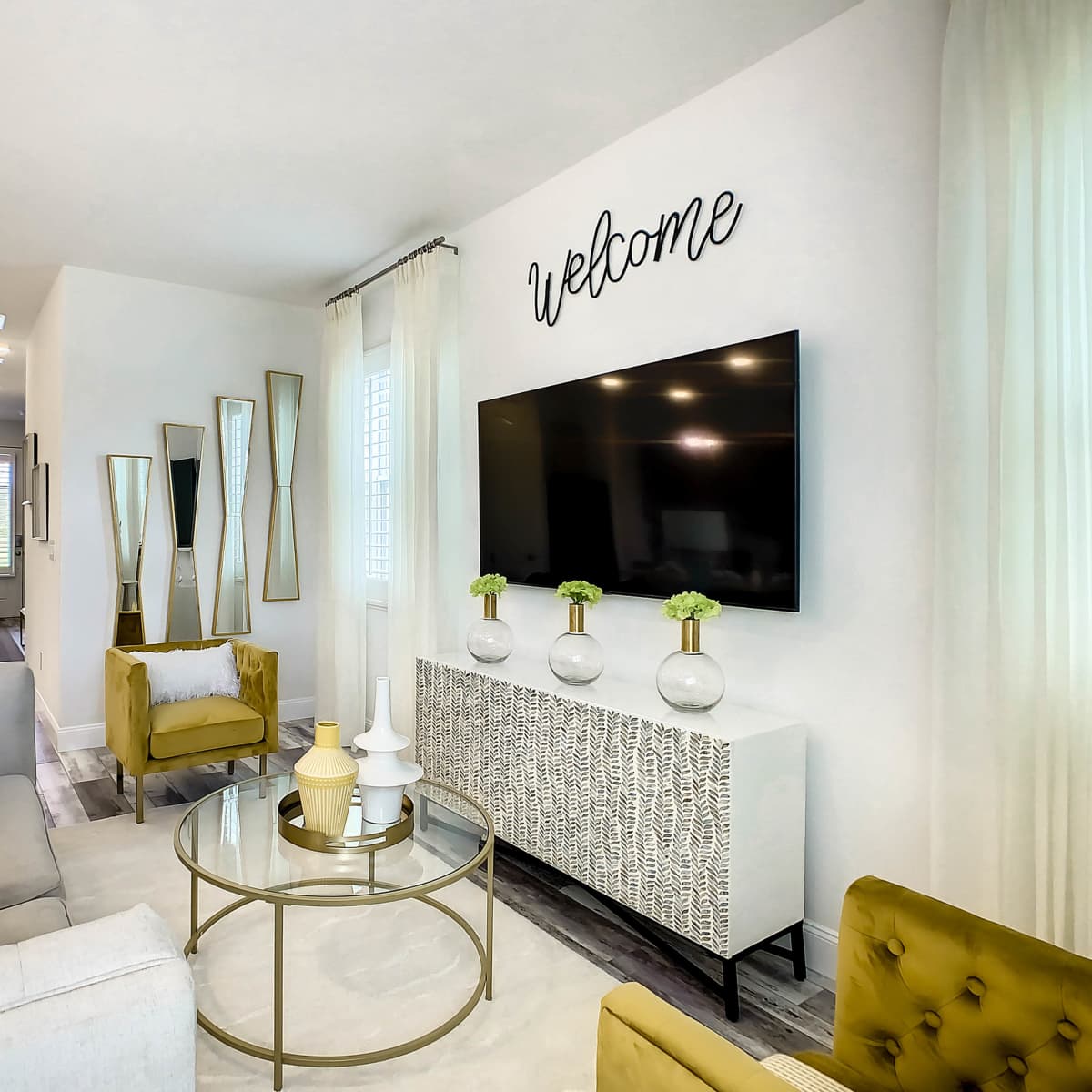 A modern living room features a large television mounted on the wall, a coffee table in the center, and a seating arrangement with a sofa and armchairs.